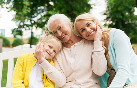 Older woman smiling on a bench with her daughter and granddaughter