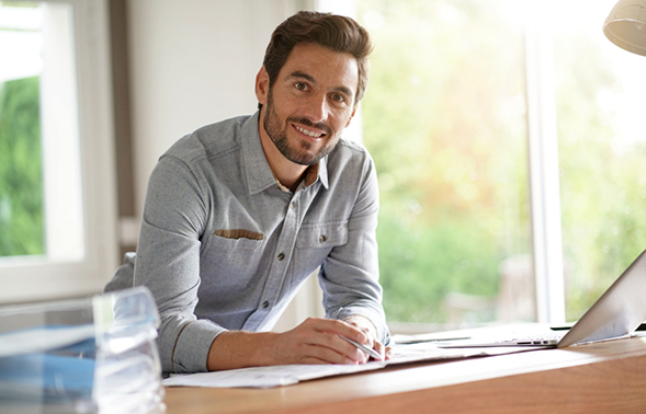 Man sitting at a desk with a pen, papers, and a laptop