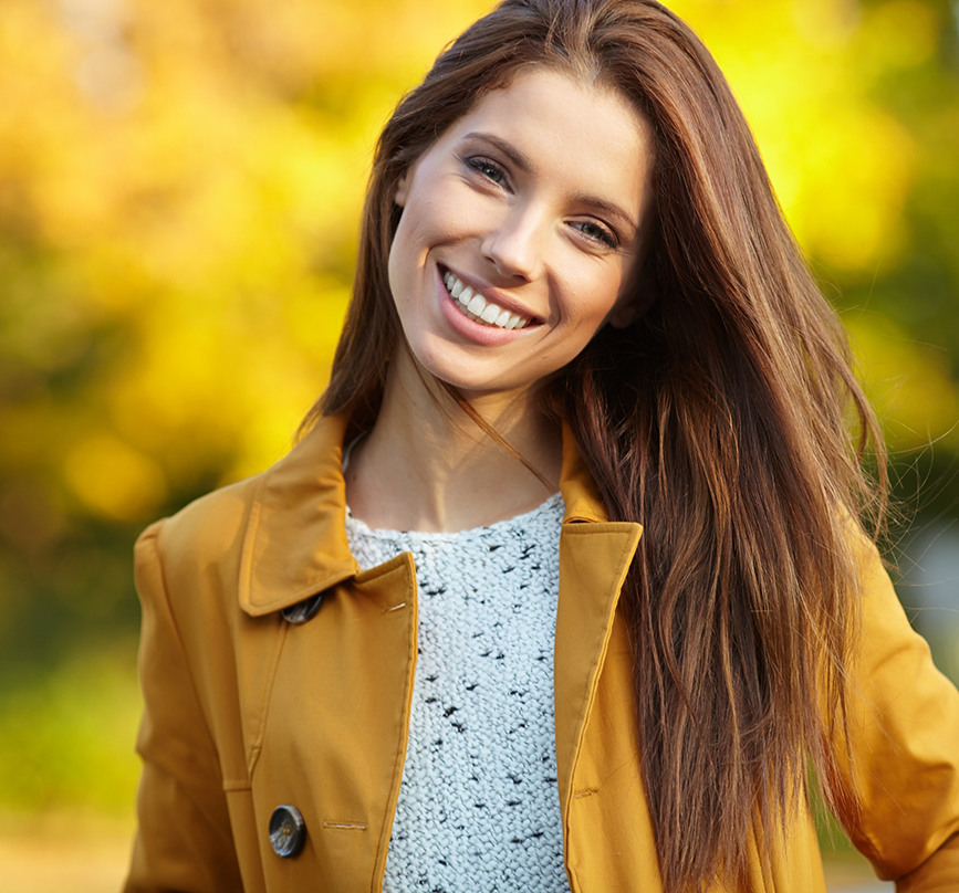 Woman in a yellow coat smiling after gum recontouring in Prosper