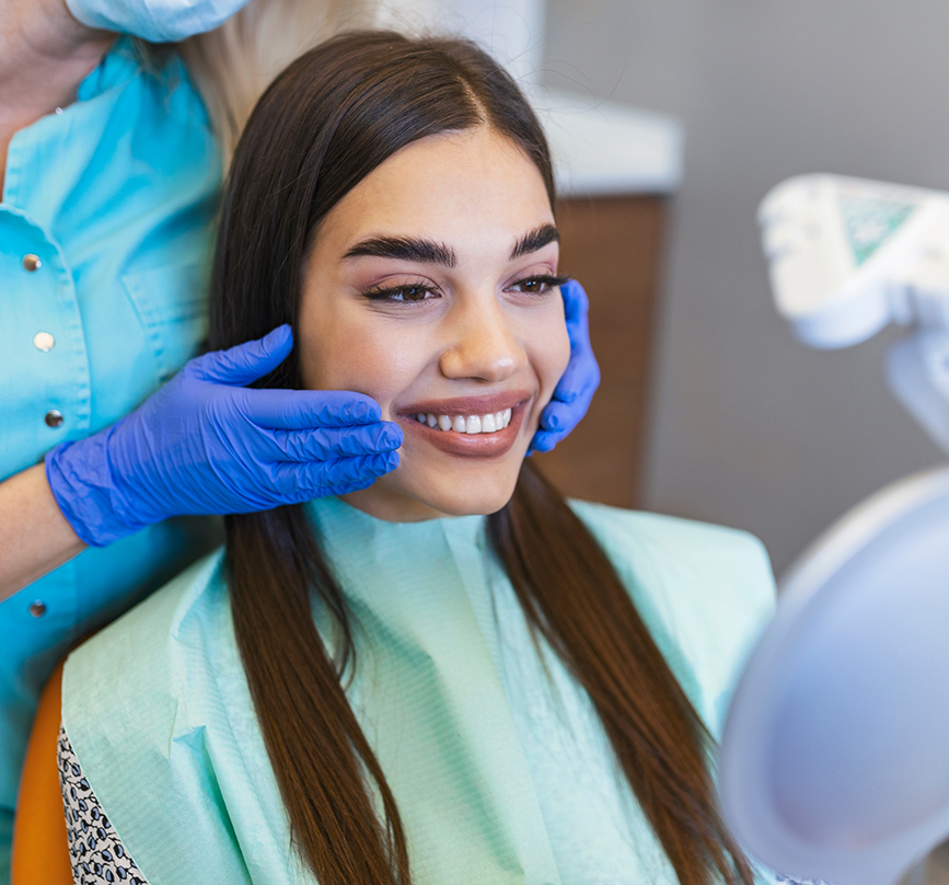 Woman looking at her smile in a mirror after receiving oral surgery services in Prosper