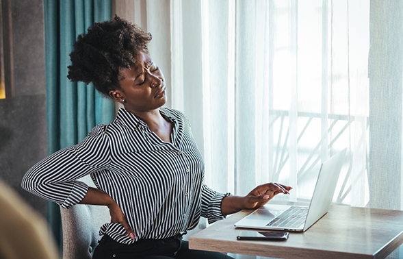 Woman at an office desk holding her lower back in pain