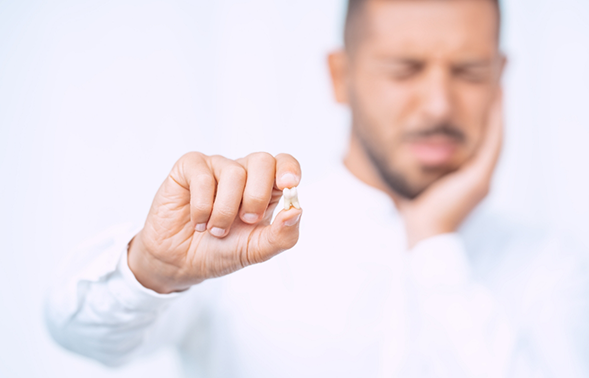 Man holding an extracted tooth in one hand and touching his cheek in pain with the other