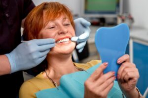 Patient with implants looking into hand-held mirror in dentist's chair.